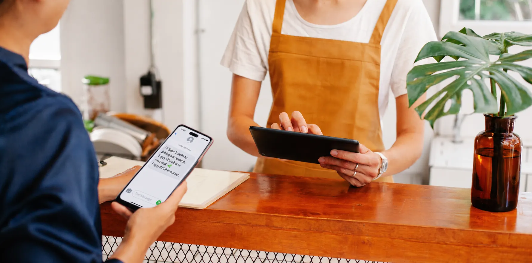 Customer reading a rewards welcome text on her phone while a staff member holds a tablet at the checkout counter