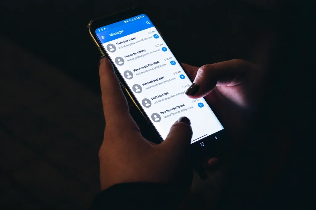 Person holding a phone at night with an inbox full of unread promotional texts from the same dispensary